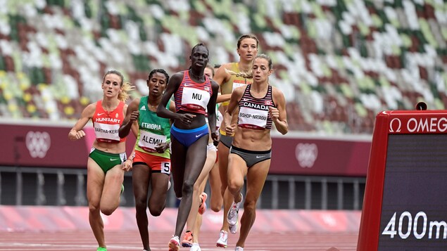 Des coureuses sont dans un virage au stade olympique de Tokyo. Les gradins sont vides derrière.