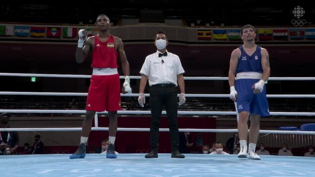 Un boxeur célèbre sa victoire sur le ring face à son adversaire dépité. Un arbitre est placé entre eux.