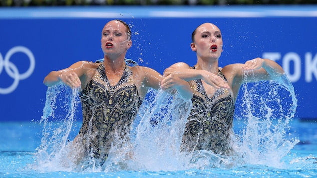 Claudia Holzner et Jacqueline Simoneau font une sortie durant leur routine. Les éclaboussures suite à leur mouvement les entourent. Les bras sont pliés avec un visage très expressif.