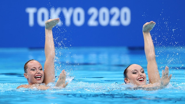Claudia Holzner et Jacqueline Simoneau de l'équipe Canada complètent leur performance lors de la natation artistique programme libre en duo. Elles ont le corps dans l'eau et les bras ainsi que la tête hors de l'eau, les deux sont parfaitement synchronisées et affichent un grand sourire.