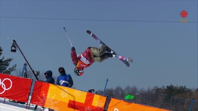 Durant un saut en pleine épreuve de demi-lune, Cassie Sharpe agrippe son ski droit derrière son dos avec sa main droite.