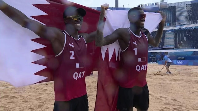 Avec un grand sourire et des lunettes de soleil, les deux joueurs de volleyball de plage du Qatar posent fièrement avec chacun leur drapeau de leur pays, qu'ils tiennent à fièrement à bout de bras.