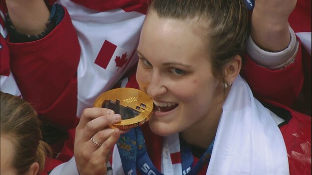 Marie-Philip Poulin, entourée de ses coéquipières, mord sa médaille d'or des Jeux olympiques de Sotchi.