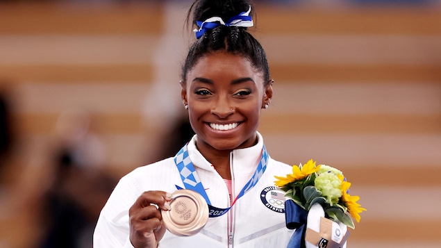 Simone Biles pose avec sa médaille de bronze à la main.
