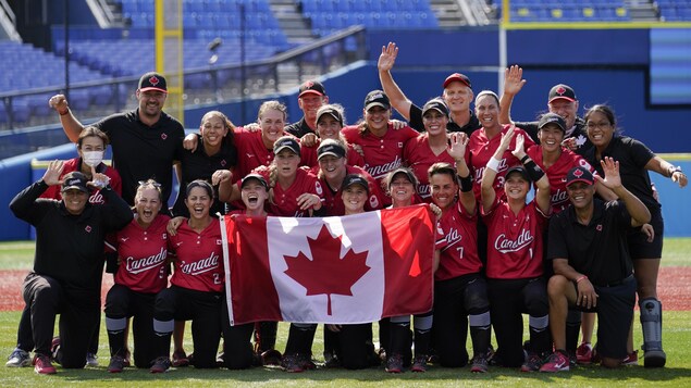 Les joueuses, les entraîneurs et le personnel de l'équipe posent fièrement avec un drapeau canadien au centre du terrain après leur victoire.