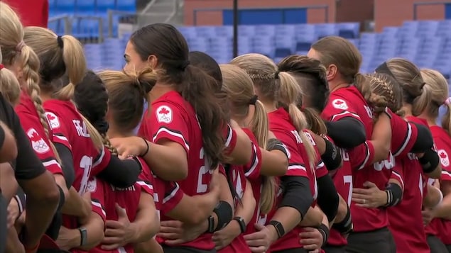 Les joueuses de l'équipe féminine de softball du Canada sont alignées, bras dessus, bras dessous.