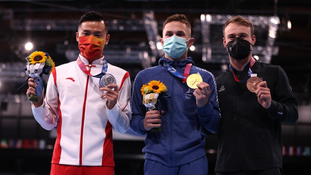 Les trois médaillés à l'épreuve du trampoline masculin, sur le podium, médailles en main.
