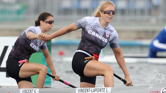 Deux canoéistes canadiennes se félicitent en se donnant la main à bord de leur embarcation.