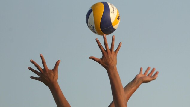 Des mains tentent d'attraper le ballon de volleyball lors d'un match. 
