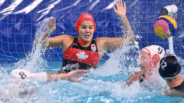 Une gardienne de but au water polo tente de garder les yeux ouverts alors qu'elle attend, les bras dans les airs, le lancer d'une adversaire.