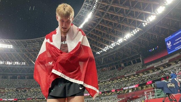Zachary Gingras porte le drapeau canadien autour de lui en regardant à terre tout en versant quelques larmes de joie aux abords de la piste d'athlétisme.
