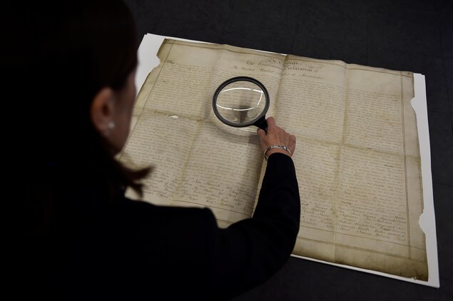 Une archiviste observe avec une loupe le parchemin de la Déclaration d'indépendance des États-Unis découvert au Royaume-Uni.