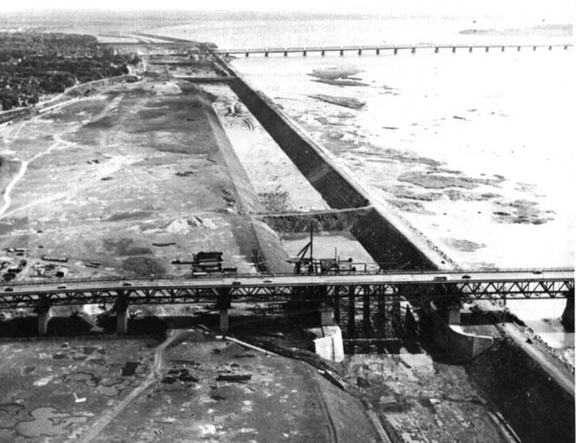 Le canal en construction, le long du fleuve, traversé par deux ponts. Le canal en construction, le long du fleuve, traversé par deux ponts.