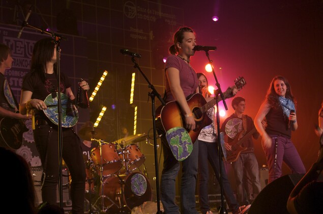 Un groupe de jeunes musiciens. Au premier plan, une guitariste et chanteuse devant son micro. Un groupe de jeunes musiciens. Au premier plan, une guitariste et chanteuse devant son micro.