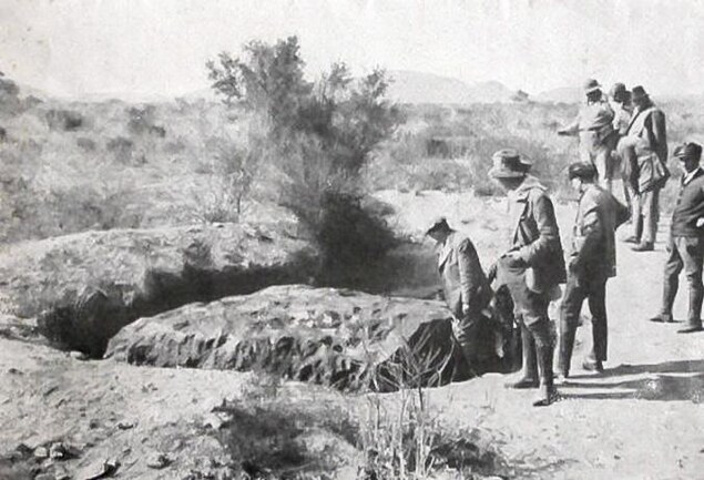 Des hommes devant un énorme fragment de météorite. Des hommes devant un énorme fragment de météorite.