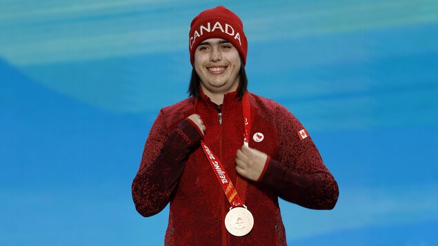 Alana Ramsay tient sa médaille sur le podium en souriant.