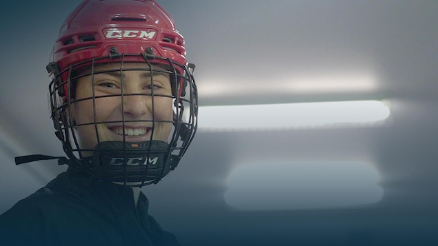 Gros plan d'une hockeyeuse qui sourit sous son casque rouge