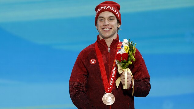 Alexis Guimond du Canada porte fièrement sa médaille de bronze et il tient un bouquet de fleur.