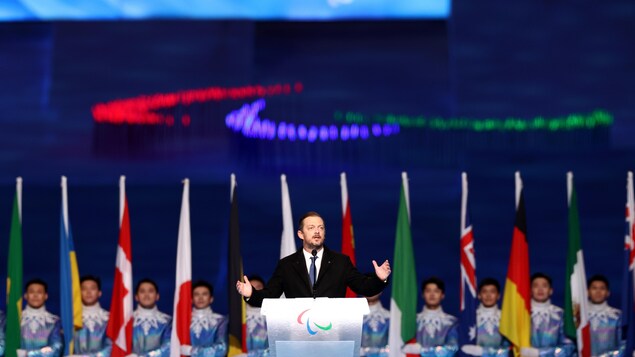 Un homme, devant des drapeaux de différents pays, prononce un discours.