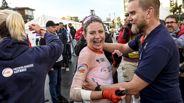La cyclise sourit à pleines dents, alors qu'un membre de son équipe s'apprête à lui faire une accolade, après la course. 