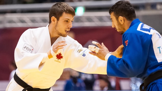 Il porte un judogi blanc et agrippe un adversaire
