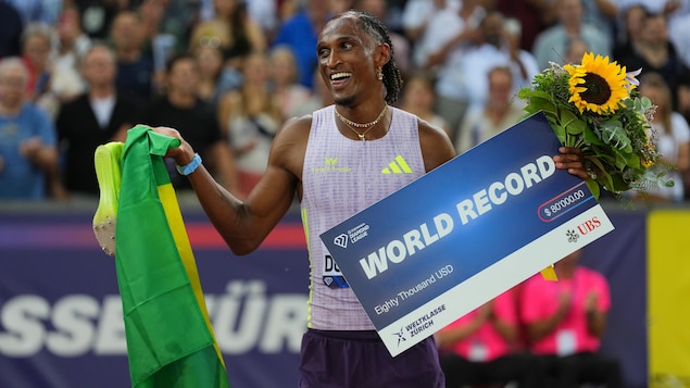 Alison dos Santos tout sourire avec un drapeau du Brésil dans une main et une affiche de record du monde dans l'autre.