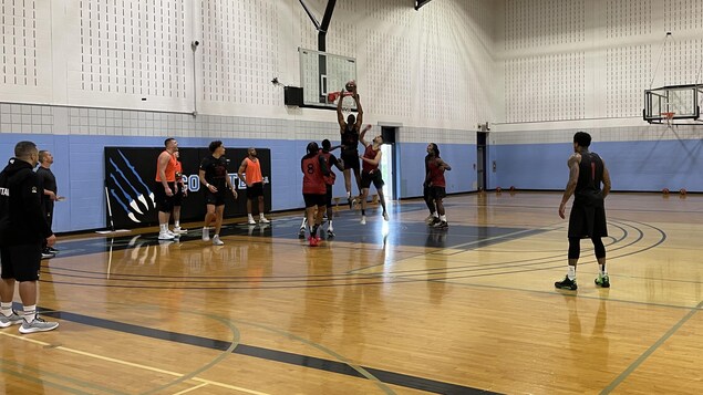 Des joueurs de basketball s'entraînent. L'un d'eux s'apprête à déposer le ballon dans le panier. 