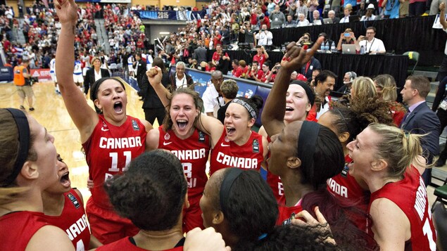 Regroupées devant le banc des joueuses et se tenant par les épaules, les membres de l'équipe canadienne de basketball féminin célèbrent leur qualification olympique.