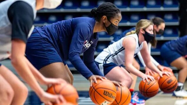 Des joueuses de basketball dribblent avec des ballons sur les lignes de côté d'un terrain.
