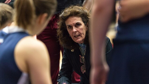 Une entraîneuse donne des directives aux joueuses de son équipe de basketball universitaire.
