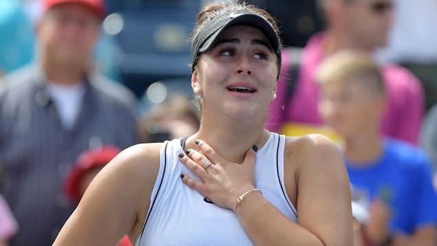 En larmes, elle porte la main à sa poitrine.