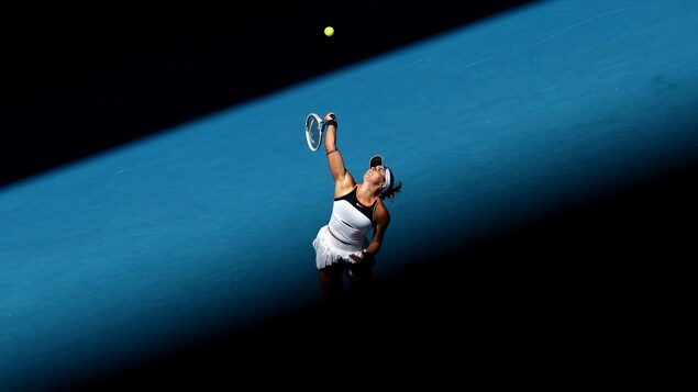 Un joueuse de tennis vêtue de blanc effectue un service lors des Internationaux d'Australie.