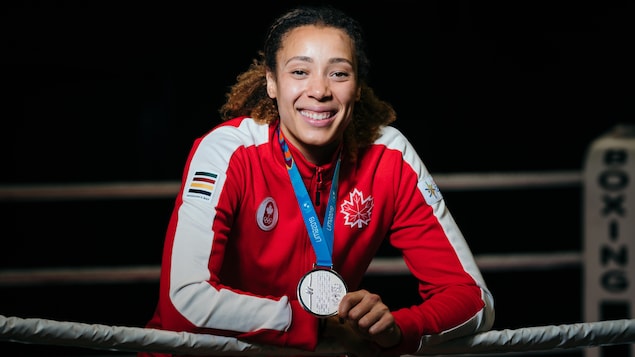La boxeuse, tout sourire, s'appuie sur le plus haut câble du ring.