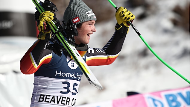 Il lève ses deux skis en l'air et affiche un large sourire.