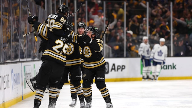 Cinq joueurs de hockey des Bruins de Boston s'enlacent pour célébrer sur la glace.