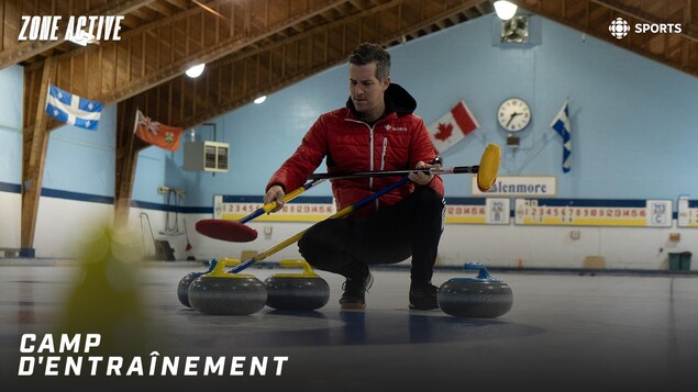 Un homme est accroupi sur la glace entouré de pierres de curling.