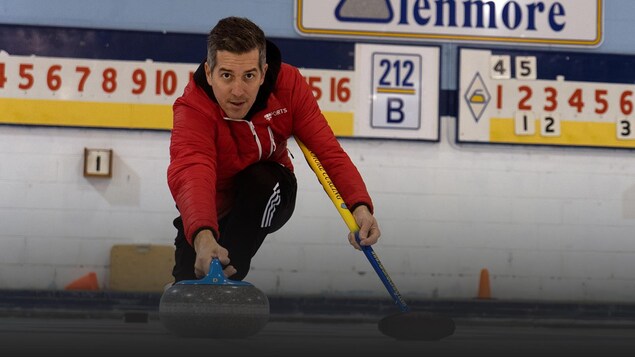 Un homme s'élance sur la glace en poussant une pierre de curling.