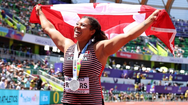 Camryn Rogers célèbre avec le drapeau canadien en main et la médaille d'argent au cou. 