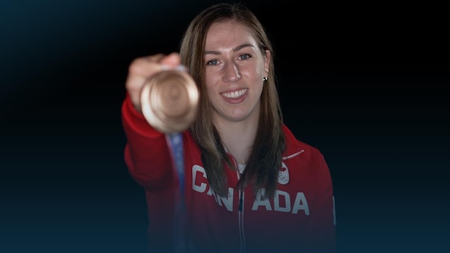 Une femme tend devant une une médaille de bronze olympique et sourit.