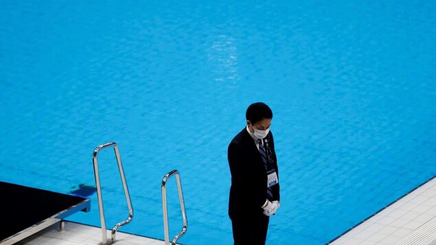 Un officiel masqué se tient devant une piscine vide