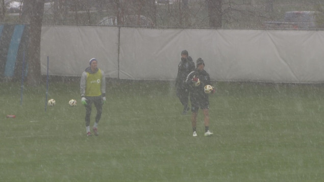 Trois hommes marchent sur un terrain de soccer en pleine tempête de neige.