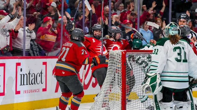 Des joueuses de hockey célèbrent un but devant une foule heureuse dans un match professionnel.