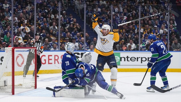 Un joueur de hockey lève les bras pour célébrer un but pendant que le gardien adverse le regarde.