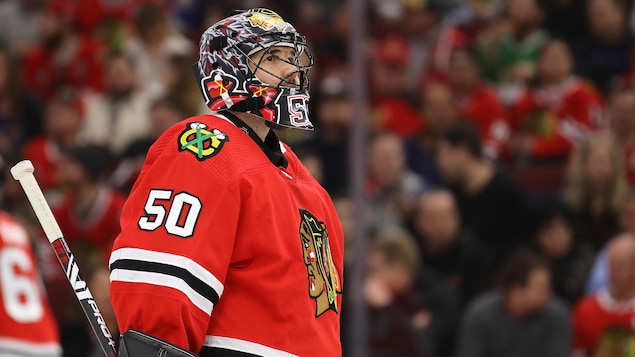 Un gardien de but de hockey devant son filet regarde au loin.