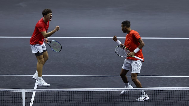 Deux joueurs de tennis, vêtus de rouge et de blanc, célèbrent un point remporté en double. 