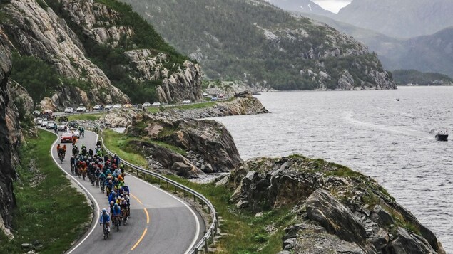 Un peloton cycliste suit une route sinueuse le long d'un fjord, en Norvège. 
