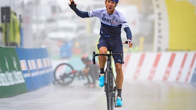 Michael Woods célèbre sous la pluie alors qu'en arrière-plan son adversaire tente de replacer son vélo.