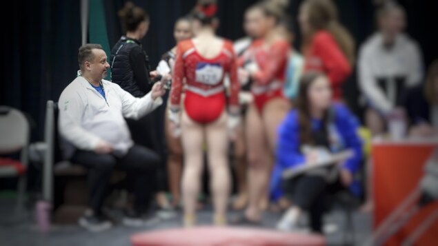 Un entraîneur parle à des gymnastes qui sont floues sur la photo.