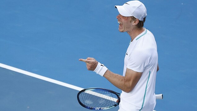 Un joueur est heureux sur un court de tennis, et pointe l'index de sa main gauche.