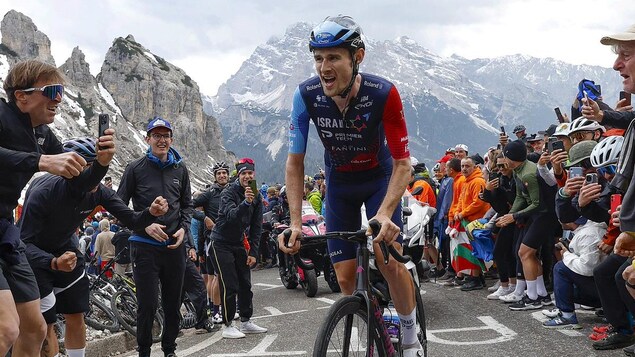 Le cycliste canadien Derek Gee est debout sur son vélo, dans une route pentue en haute montagne.
